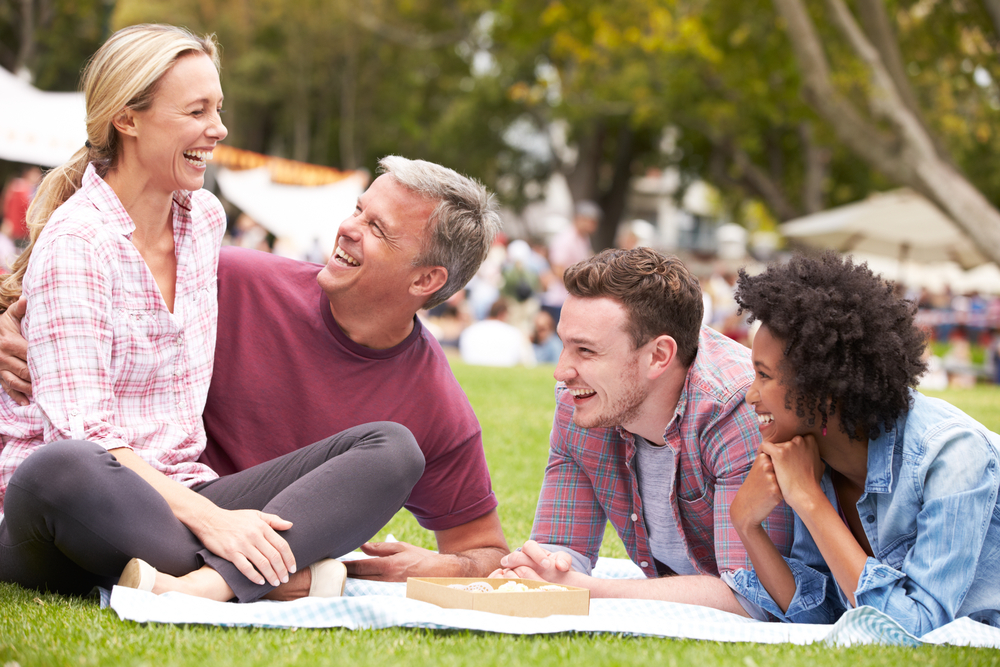 parents with their adult son and his girlfriend sitting in a park and laughing